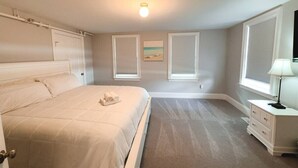 A bedroom with a bed, a nightstand, a lamp, and two windows with blinds.