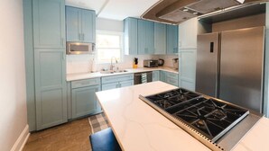 A modern kitchen with light blue cabinets, stainless steel appliances, and a white marble countertop.