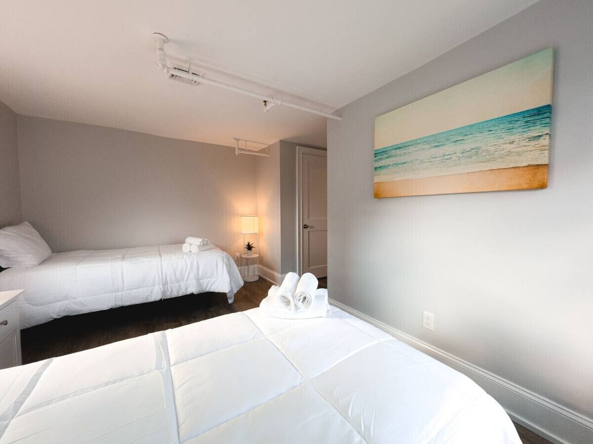 A hotel room with two beds, a painting of a beach, and a nightstand with a lamp.