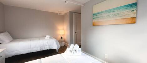 A hotel room with two beds, a painting of a beach, and a nightstand with a lamp.