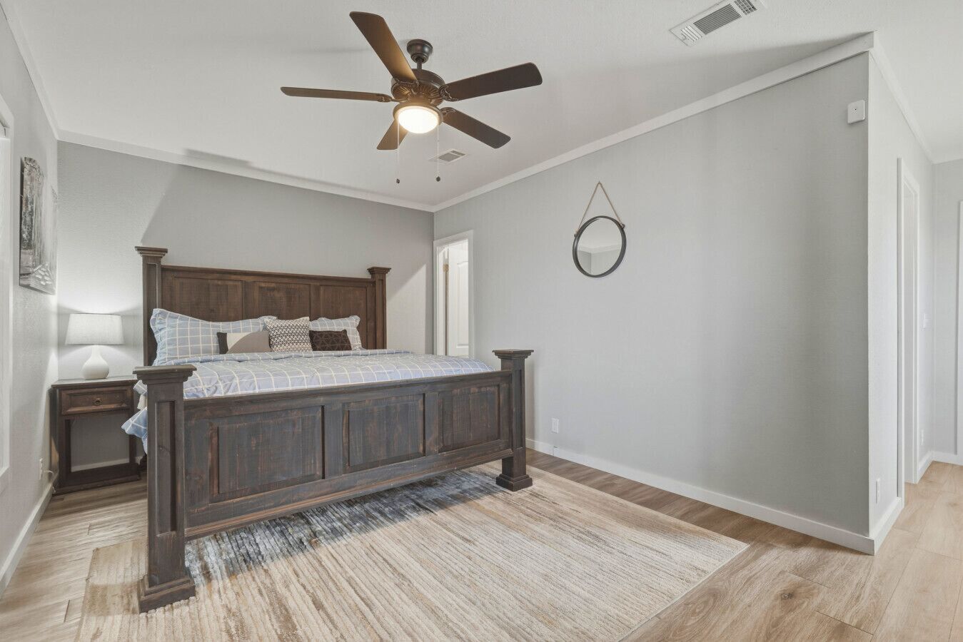 A bedroom with a bed, a nightstand, a ceiling fan, a rug, and a wall-mounted mirror.