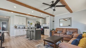 A modern kitchen with white cabinets, a central island with stools, a ceiling fan, and a brown leather sofa with a patterned rug. - Lake Front Lake House Paradise! (Pittsburg)