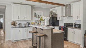 A kitchen with white cabinets, a wooden island with stools, a refrigerator, a stove, and a microwave. - Lake Front Lake House Paradise! (Pittsburg)