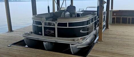 A pontoon boat docked at a wooden pier with a covered area overhead.