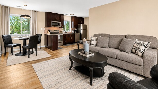 A modern kitchen with dark wood cabinets, a central island, and a dining area with a round table and chairs.