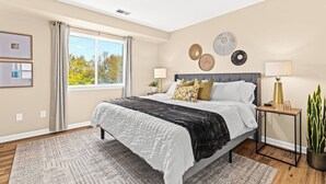 A modern bedroom with a large bed, a bedside table, a nightstand, and a window with curtains.
