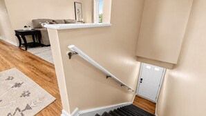 A staircase with a handrail, a wooden floor, a beige wall, and a door at the bottom.