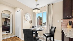 A modern kitchen with a dining area, a large window with curtains, and a view of the outdoors.