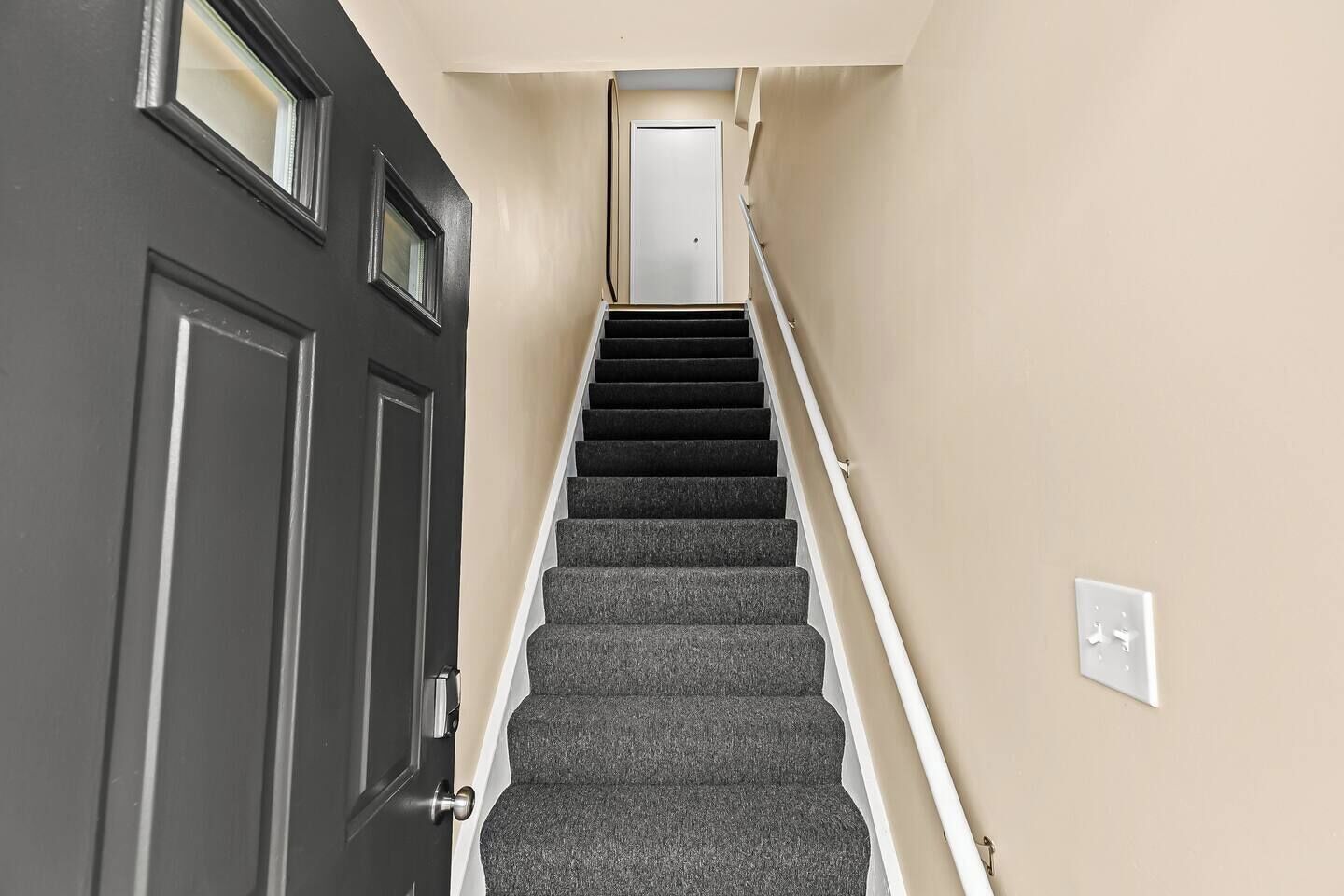A staircase with carpeted steps leading to a door with a small window.