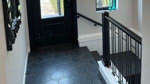 Un pasillo moderno con una puerta negra, una escalera con barandilla negra y una lámpara en el techo.