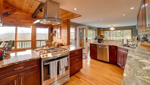 A spacious kitchen with wooden cabinets, granite countertops, stainless steel appliances, and large windows offering views of the outdoors.