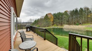 A deck with outdoor furniture, a pond, and a forested area.