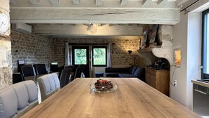 A rustic dining room with a wooden table, leather chairs, and a stone wall. - Gite Climatisé les Lauriers (Essey)