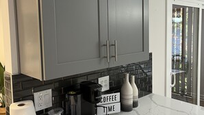 Eine Küche mit grauen Schränken, einer Marmorarbeitsplatte, einer Kaffeemaschine und einem Schild mit der Aufschrift 'COFFEE TIME'.