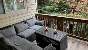 Eine überdachte Außenbereich-Sitzgelegenheit mit einer Couch und einem Tisch, umgeben von einem Holgitter und Blick auf Bäume.