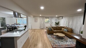 Ein modernes Wohnzimmer mit einem großen, braunen Ecksofa, einem Essbereich mit einem Glastisch und einer Küche mit Kochinsel.