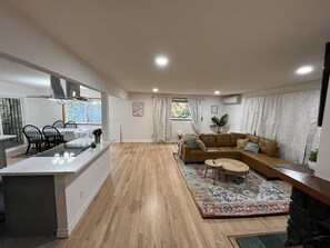 Un soggiorno moderno con un ampio divano angolare marrone, una zona pranzo con tavolo in vetro e una cucina con isola centrale.
