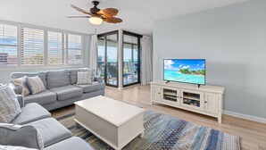 Ein Wohnzimmer mit grauem Sofa, weißem Couchtisch und einem Fernseher auf einem weißen Schrank.