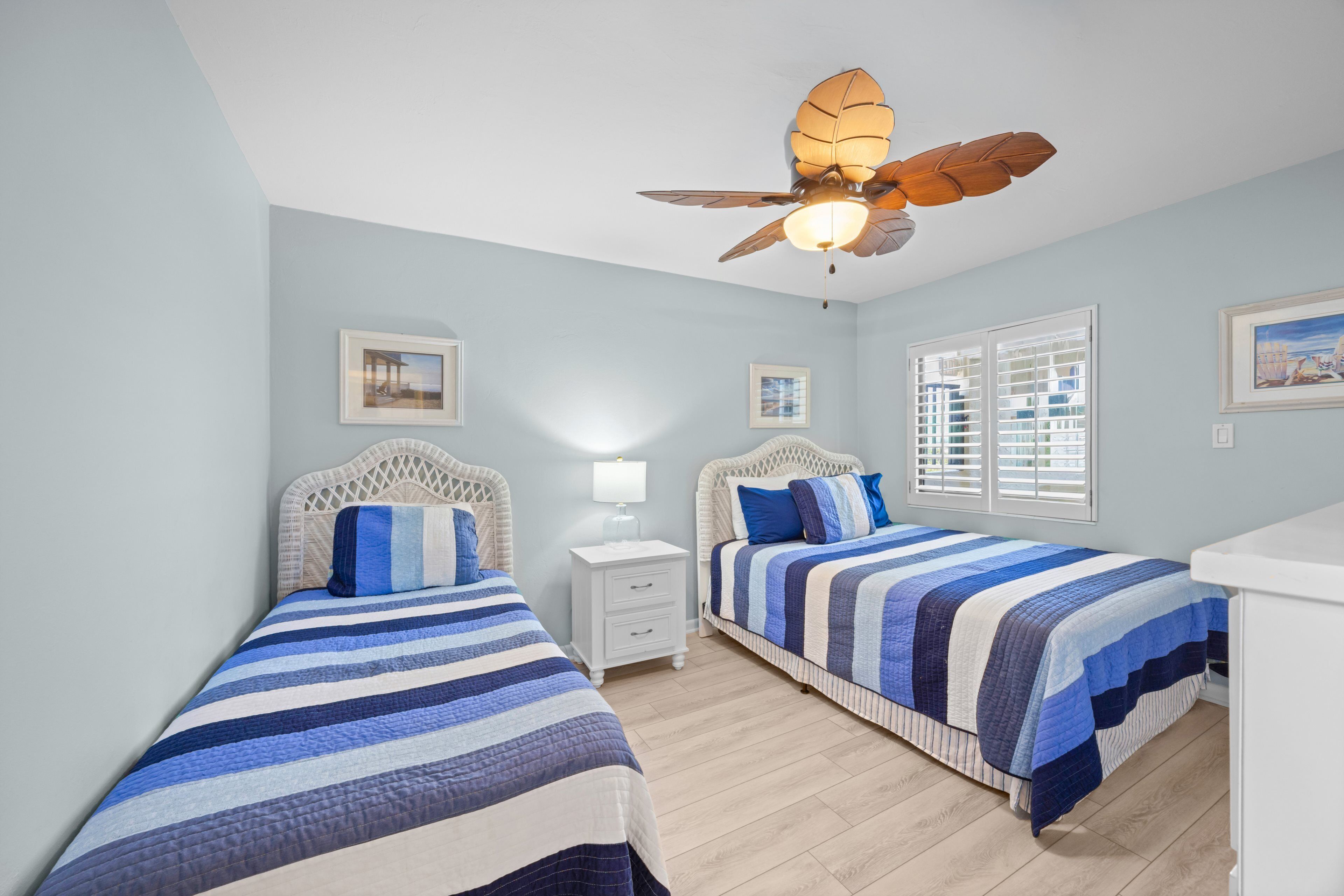 A bedroom with two beds, a ceiling fan, a nightstand, and a window with shutters.