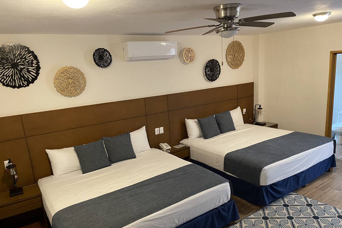 Una habitación de hotel con dos camas, ventilador de techo, aire acondicionado y decoración en las paredes.