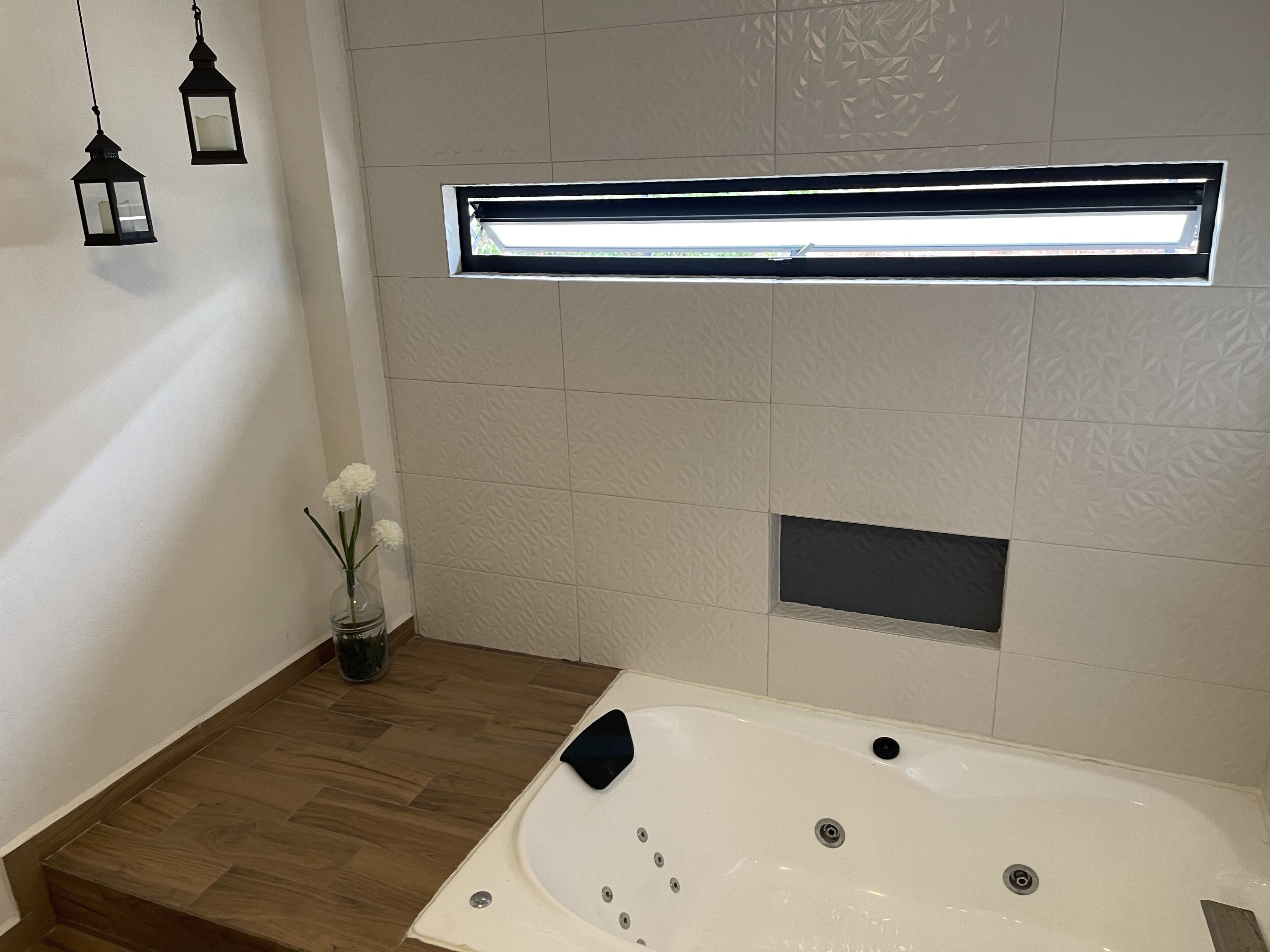 A modern bathroom with a freestanding bathtub, a small window with a light fixture, and a decorative vase with flowers.