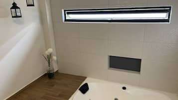 A modern bathroom with a freestanding bathtub, a small window with a light fixture, and a decorative vase with flowers.