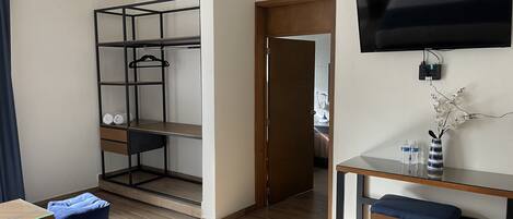 A modern room with a wooden floor, a TV mounted on the wall, a desk with a bench, and a metal shelving unit with a hanging rack.