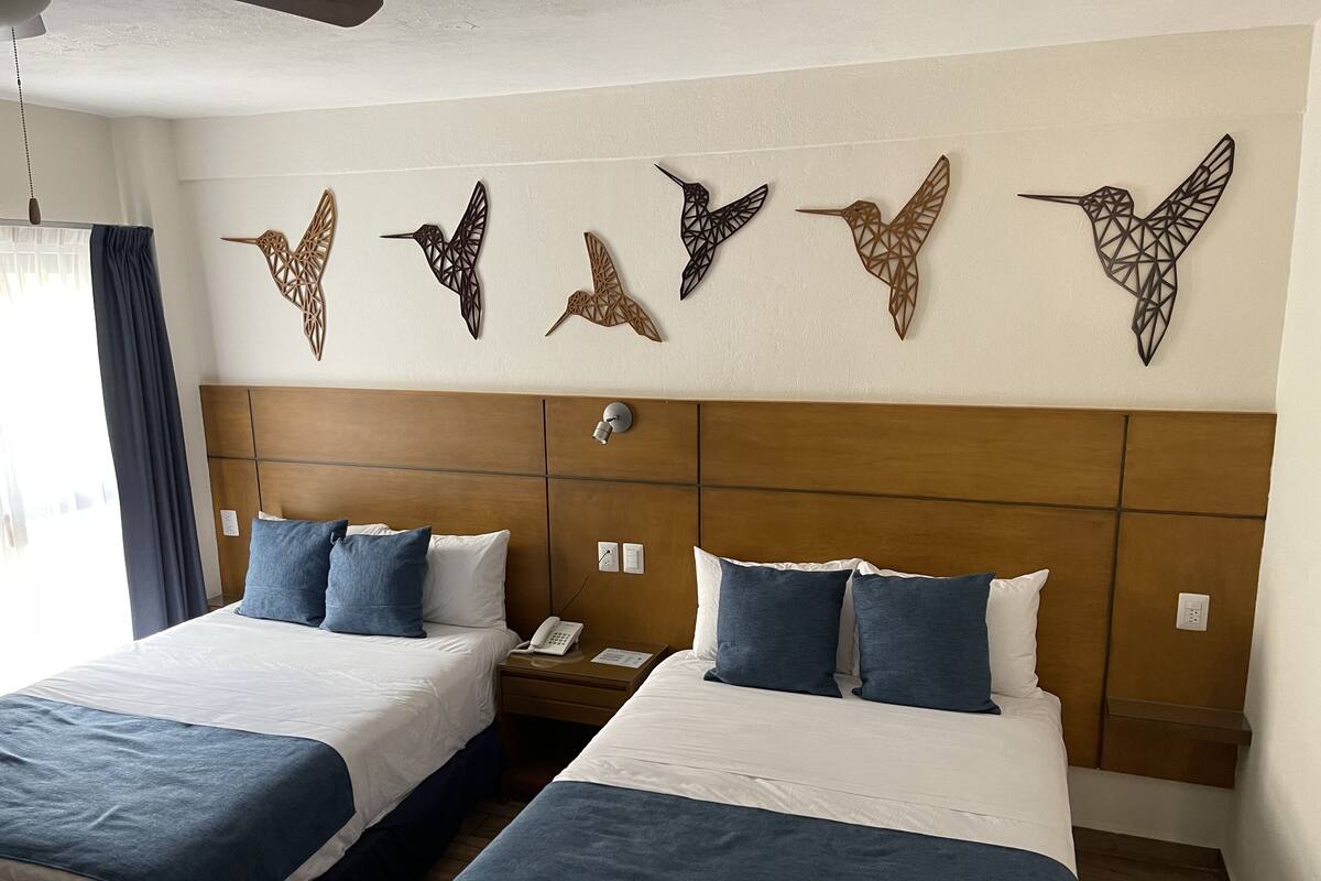 Habitación de hotel con dos camas, cabecero de madera, teléfono montado en la pared y decoración de pájaros en la pared.