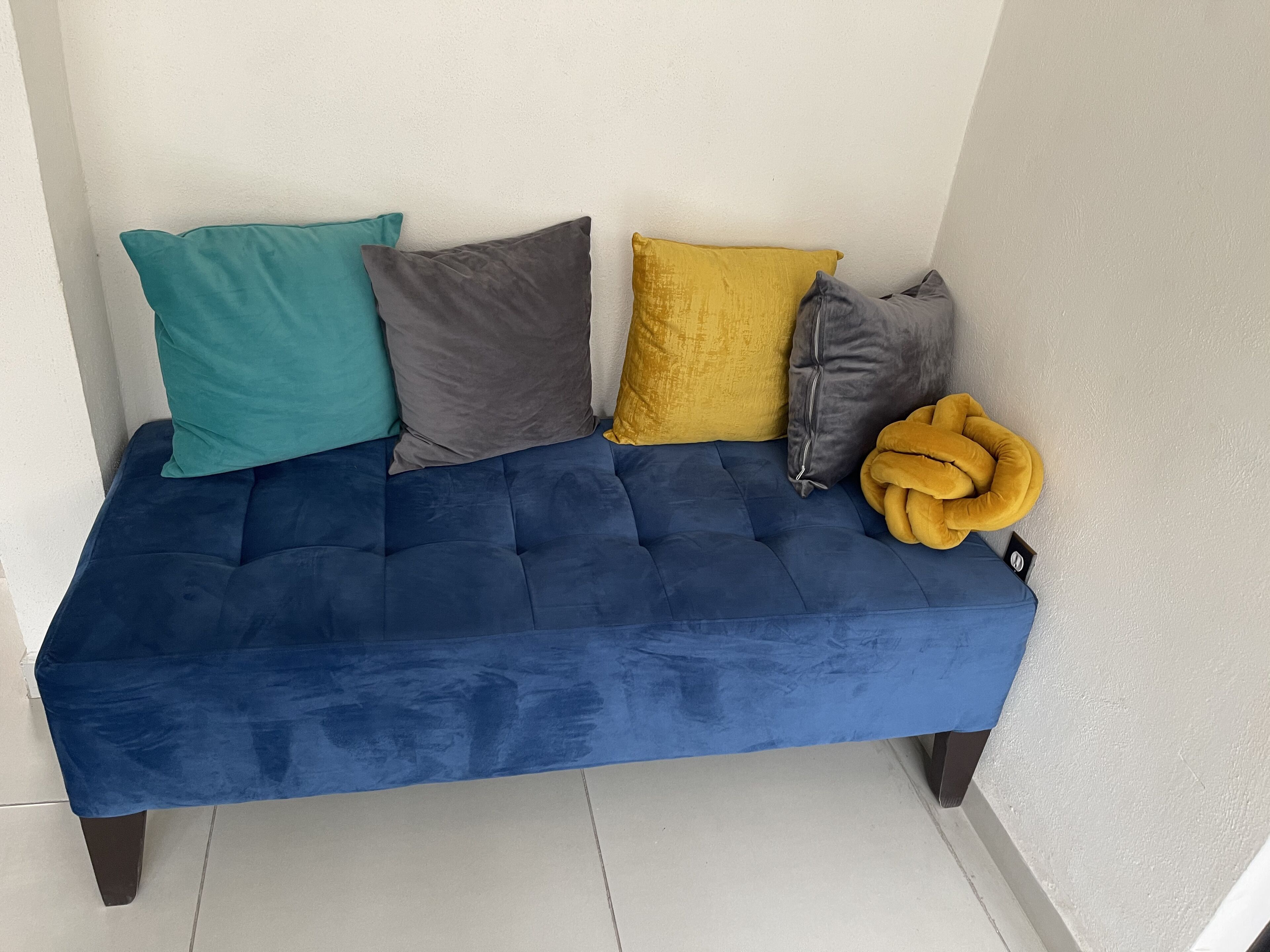 Un sofá azul con cuatro cojines en tonos turquesa, gris, mostaza y gris.
