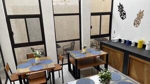 Un comedor moderno con mesas y sillas de madera, individuales azules y una encimera de cocina con varios recipientes.