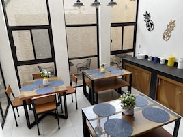 Un comedor moderno con mesas y sillas de madera, individuales azules y una encimera de cocina con varios recipientes.