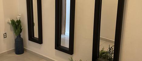 Three black-framed mirrors on a wall, a potted plant, and a woven basket with greenery.