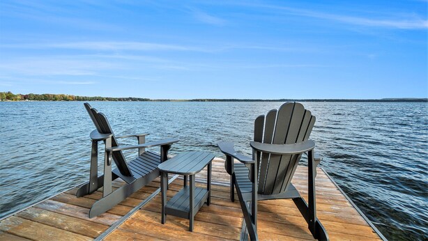 A wooden dock with two Adirondack chairs and a small table, overlooking a calm lake with a distant shoreline. - South Shore Bear Lake Family Cottage (Bear Lake)