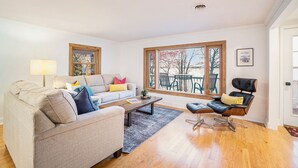 A living room with a sofa, a coffee table, a black chair, and a large window with a view of trees. - South Shore Bear Lake Family Cottage (Bear Lake)