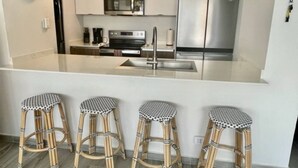 A modern kitchen with a central island, stainless steel appliances, and three wicker stools. - OT7-3 bedrooms near to everything (Carolina)