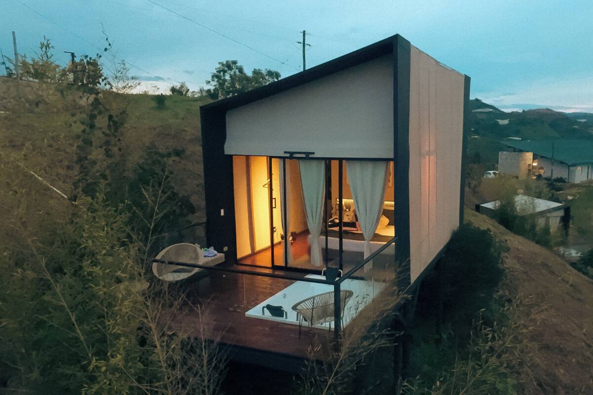 Una casa moderna de dos pisos con balcón, rodeada de vegetación natural.