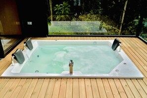 A rectangular hot tub with four jets on a wooden deck, surrounded by glass walls with a view of dense foliage. - Luum Glamping by Roots Rentals (Marinilla)
