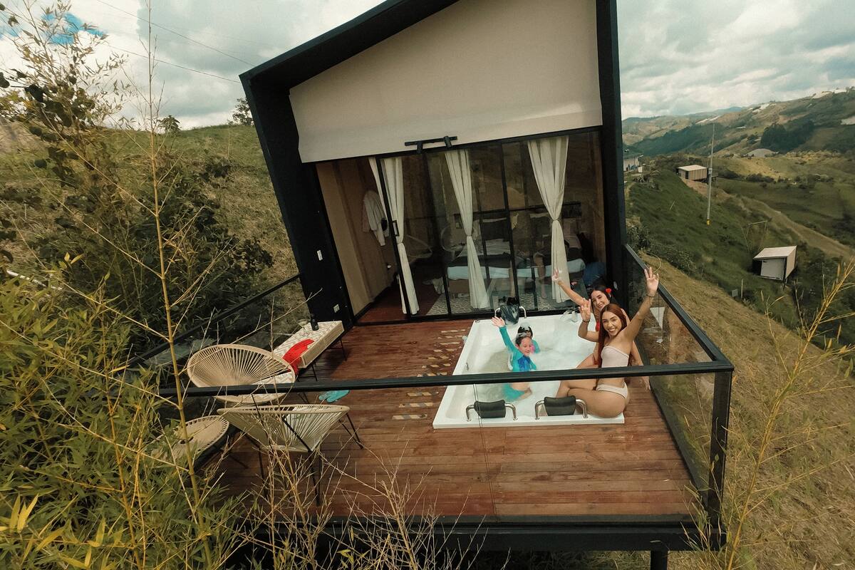 Un área moderna de hidromasaje al aire libre con un deck de madera, rodeada de exuberante vegetación y con vistas a un paisaje montañoso.