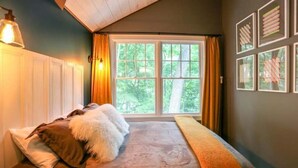 A cozy bedroom with a large window, a bed with a fluffy pillow, and a wall-mounted lamp. - Updated cottage "Beriozka" on Cedar Lake (Chester)