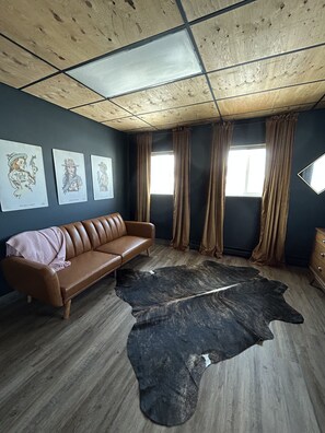 Una habitación con un sofá de cuero marrón, un tapete de cuero negro y tres obras de arte colgadas en la pared.
