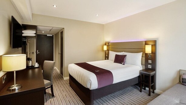 A hotel room with a bed, bedside tables, a desk with a lamp, a chair, and a TV mounted on the wall. - Premier Inn Dover Central (Dover)