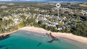 Vue aérienne d’une zone résidentielle côtière, avec des maisons, une plage et un ciel dégagé.