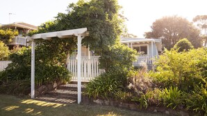 Un jardin agrémenté d’une pergola blanche, d’une végétation luxuriante, et avec une maison en arrière-plan.
