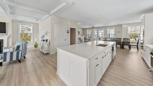 A spacious kitchen with a large island, a dining area with a table and chairs, and a living room with a sofa and a fireplace. - Fenwick on Bay mins to beach. Hot tub, Game Rm! (Selbyville)