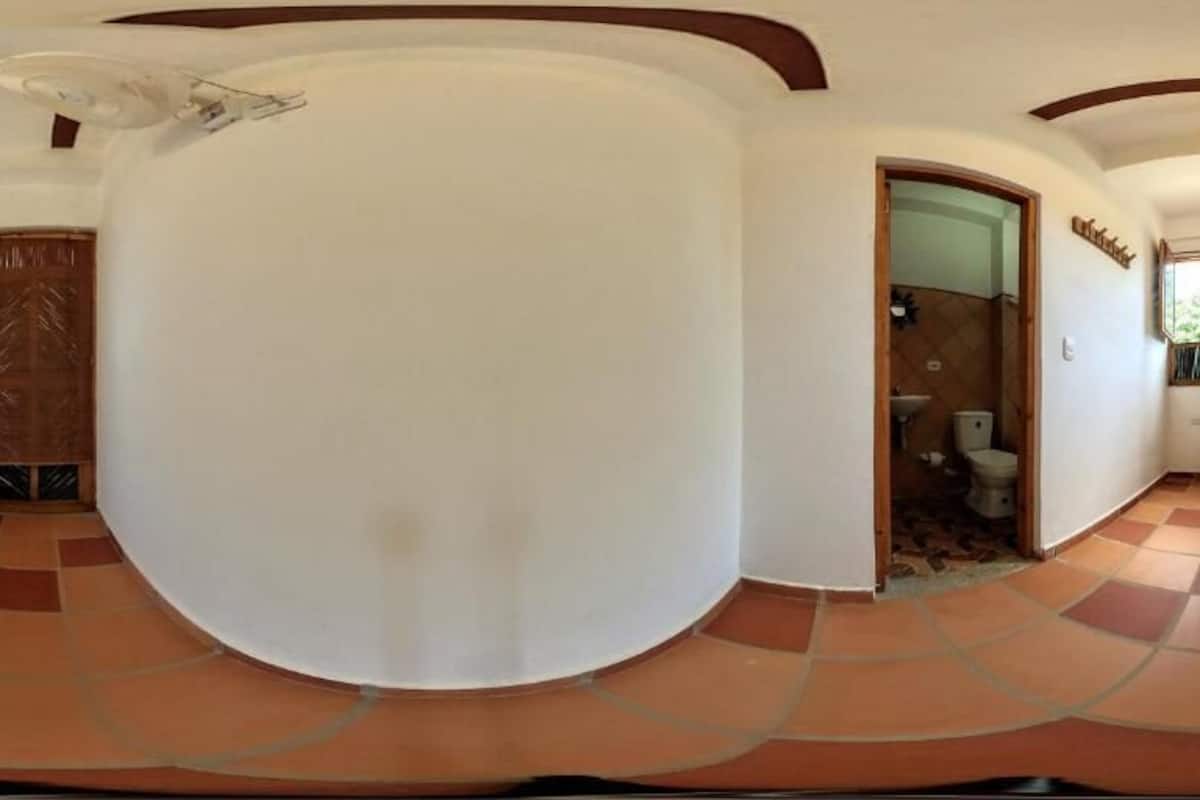Una habitación amplia con techo curvo, una cama, una puerta de madera y un baño visible a través de un vano abierto.