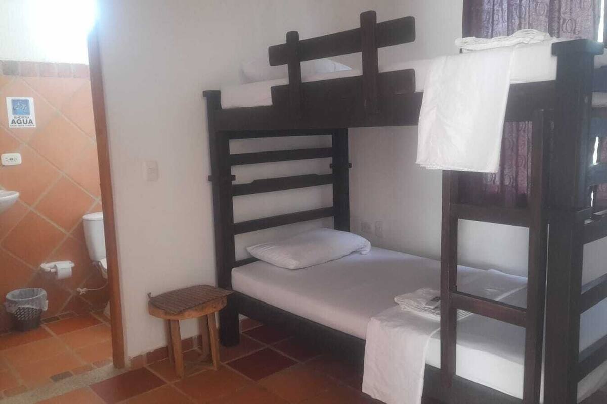 Habitación con literas, un taburete de madera y una toalla blanca colgada de la litera.