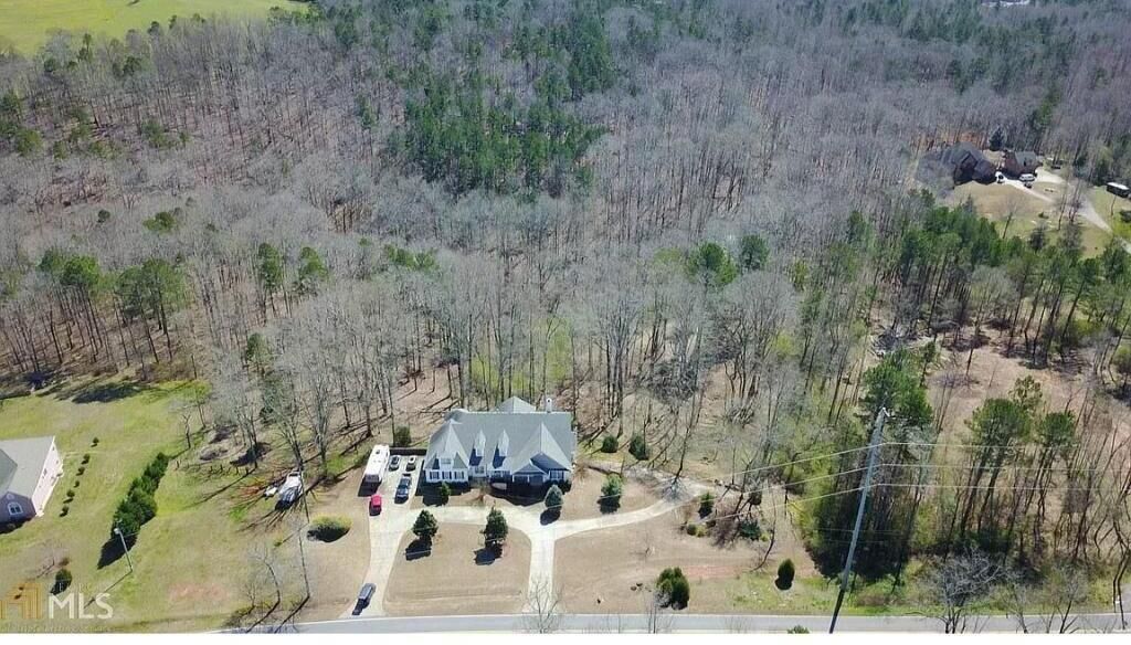 An aerial view of a residential property with a large house, multiple cars, and surrounding trees.
