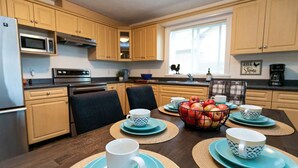 Une cuisine moderne avec des meubles en bois, un four à micro-ondes et une cuisinière. On y trouve une table à manger dressée avec des assiettes, des tasses bleues et blanches, et un saladier rempli de pommes.