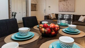 Un coin repas avec une table dressée pour quatre personnes, un saladier de pommes et un miroir accroché au mur.