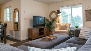 Un salon avec un téléviseur, un miroir rond, un fauteuil et un canapé.